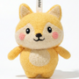 Front view of a handmade Woobbi fox keychain, made from soft yellow and cream wool felt. The fox has pointed ears, rosy pink cheeks, and a happy smiling face with black eyes and nose. It features a white belly patch and is attached to a black metal keyring with a tag labeled 'Woobbi'. The background is plain white.