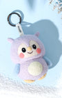 Front view of handcrafted needle-felted wool owl bag charm in purple and blue, featuring a cute smiling face and white branded Woobbi tag, styled on a winter blue background.