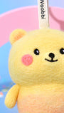 Macro close-up of needle-felted bear face showing the fuzzy Merino wool texture, hand-stitched smile, and rosy pink cheeks.
